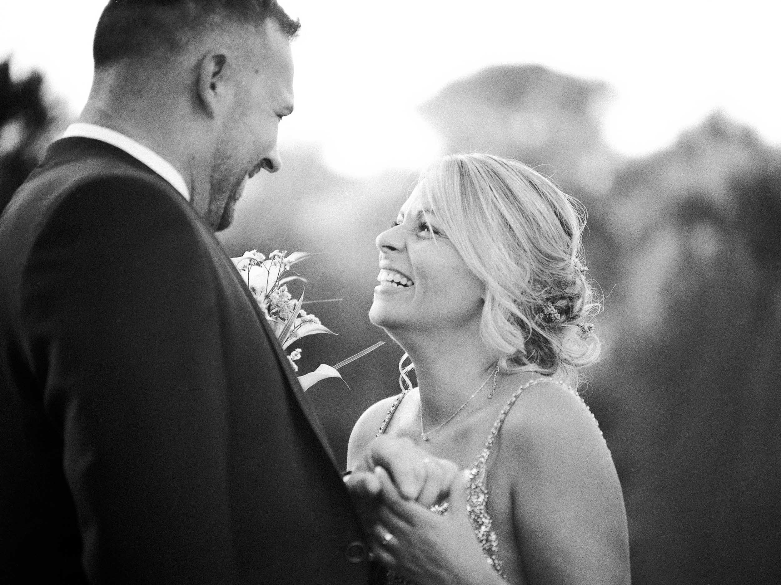 A man in a dark suit and a blonde woman in a sparkly dress laugh together in warm golden light, Reme and Aleix’s wedding