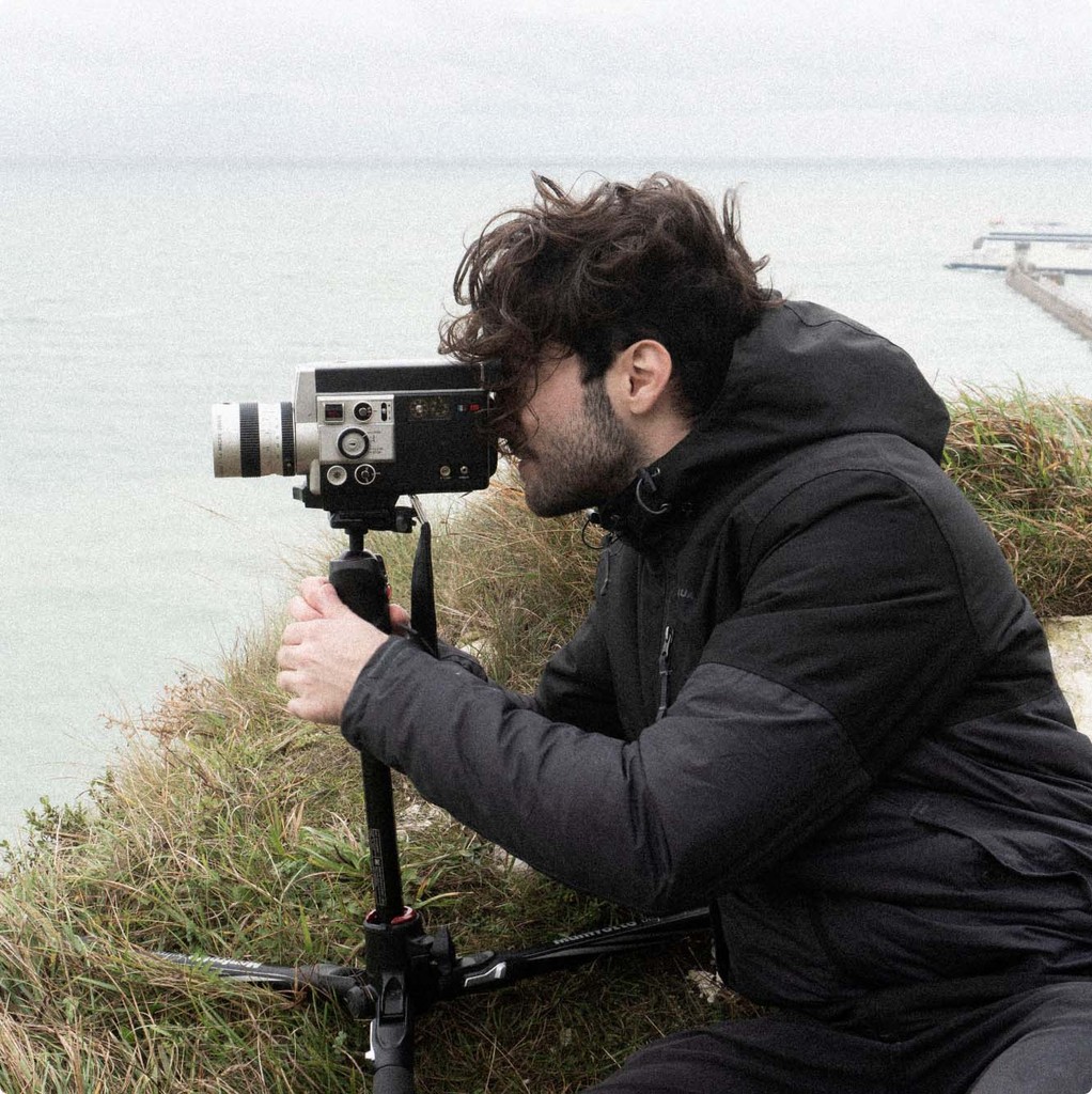 Martí Llavina filming with a vintage film camera on a coastal cliff