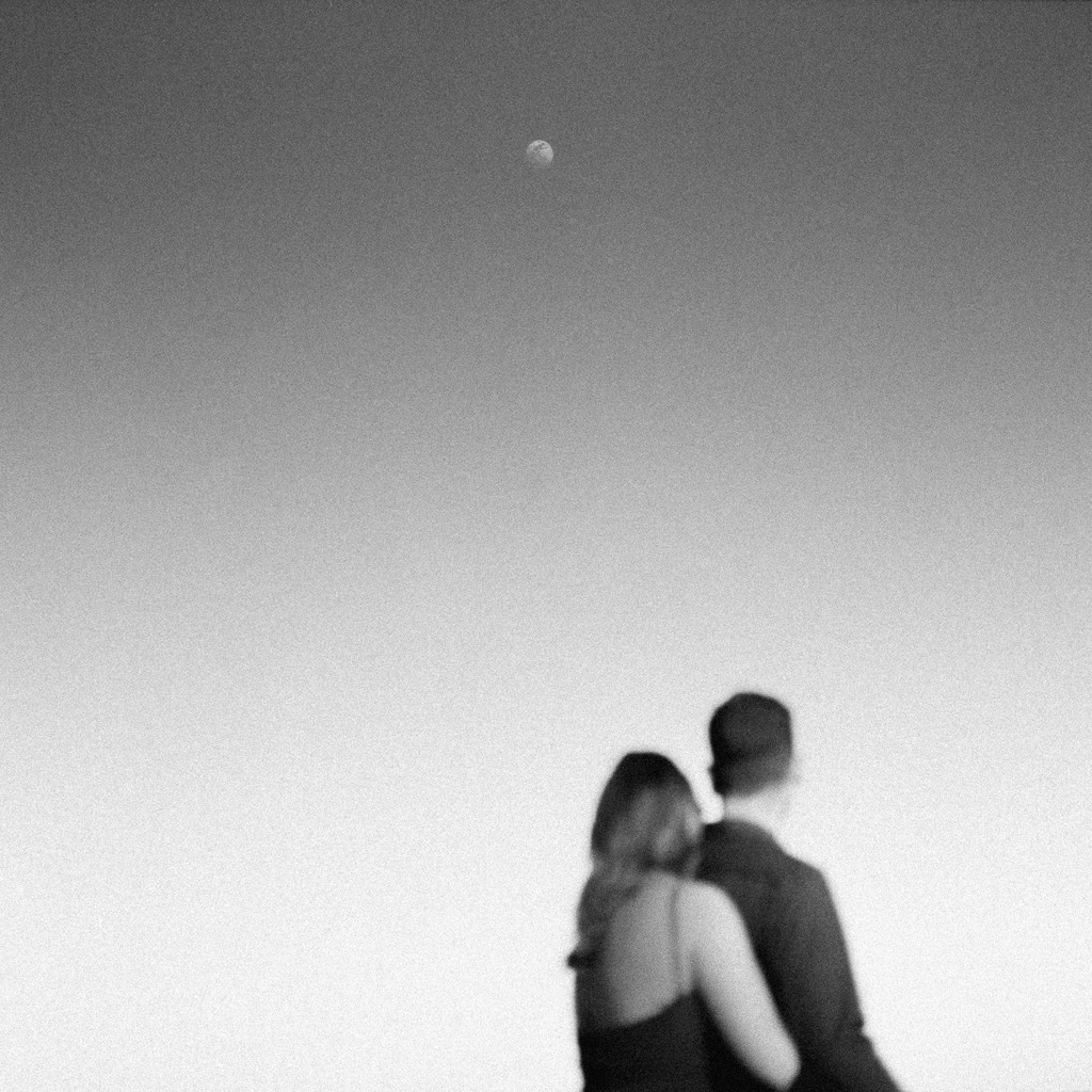 Black and white shot of the couple embracing against a pale sky with a faint moon, wedding photography in Catalonia