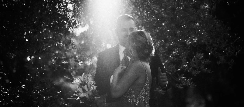 Couple embracing in black and white with sunlight through the trees, fine art wedding photography