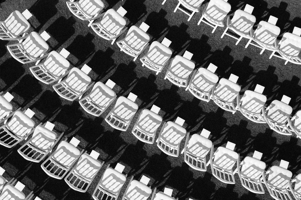 Black and white overhead view of rows of white folding chairs forming a bold diagonal pattern, wedding photography in Catalonia