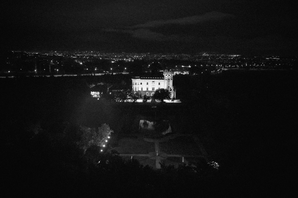 Dark night aerial view of a lit villa and distant town lights across a black landscape, wedding photography in Catalonia