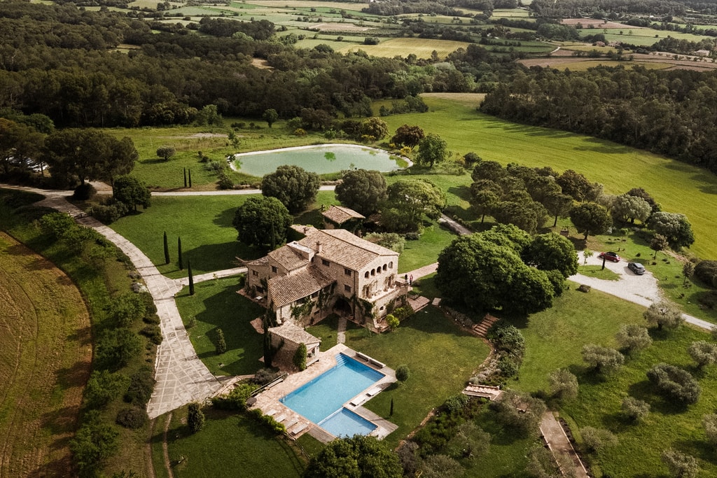 Aerial view of a country estate with a stone farmhouse, swimming pool, lawns and green fields, wedding photography in Catalonia