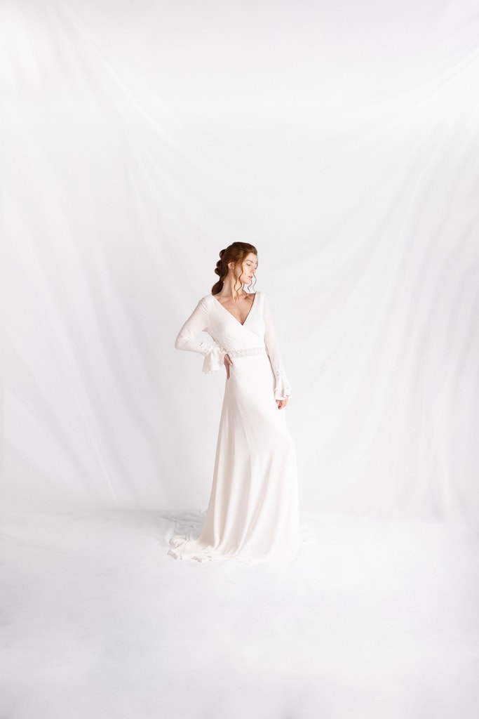 The bride alone in a long-sleeved white gown against a plain white draped backdrop, wedding photography in Catalonia