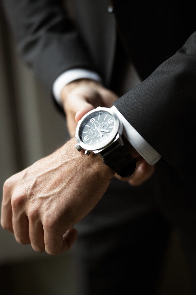 Close-up of the groom’s wristwatch on his wrist, dark suit sleeve, moody light, wedding photography in Catalonia
