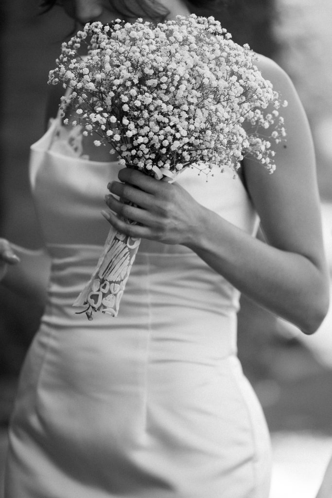 Black and white shot of the bride’s satin dress with a baby’s breath bouquet held at her side, wedding photography in Catalonia