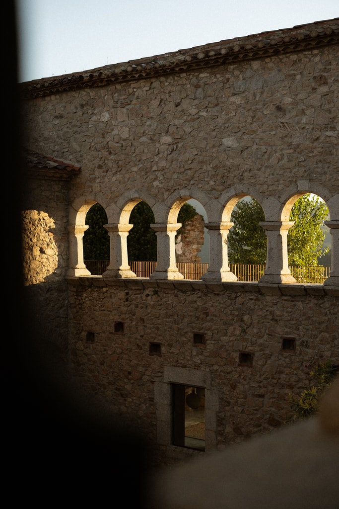 Sunlit stone cloister arches seen from a dark foreground, golden light on old walls, wedding photography in Catalonia