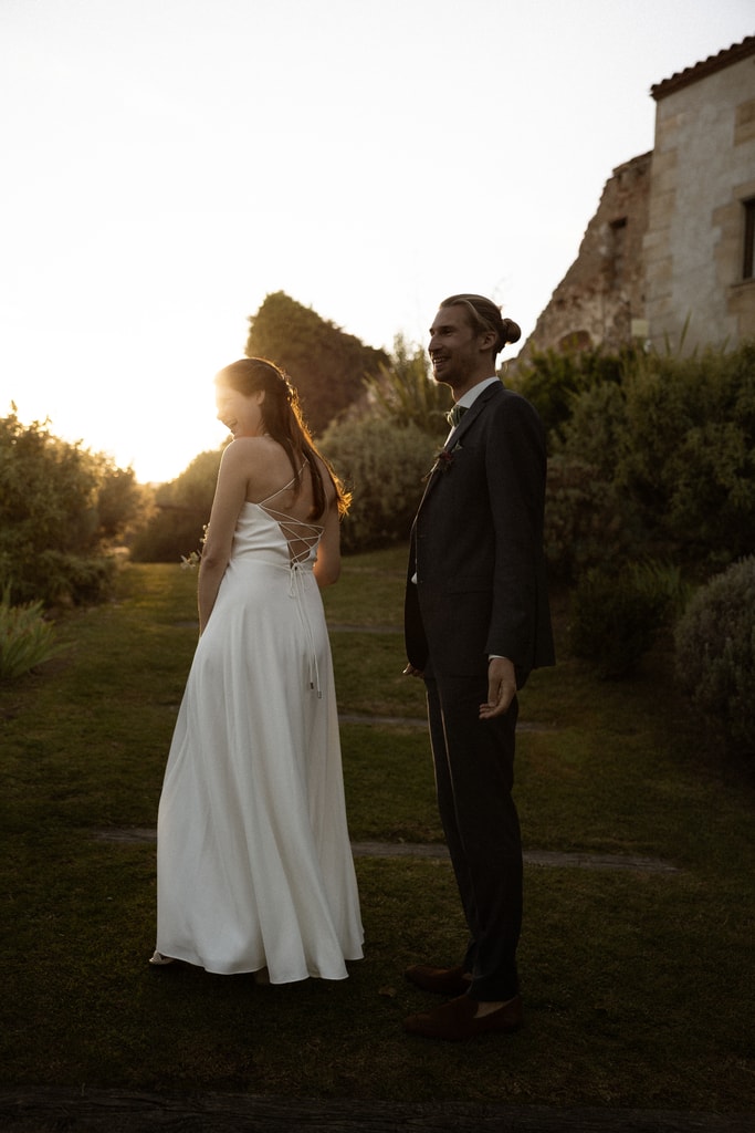 The couple stand in a garden in golden evening light, mountains behind, bride in a long white dress, wedding photography in Catalonia