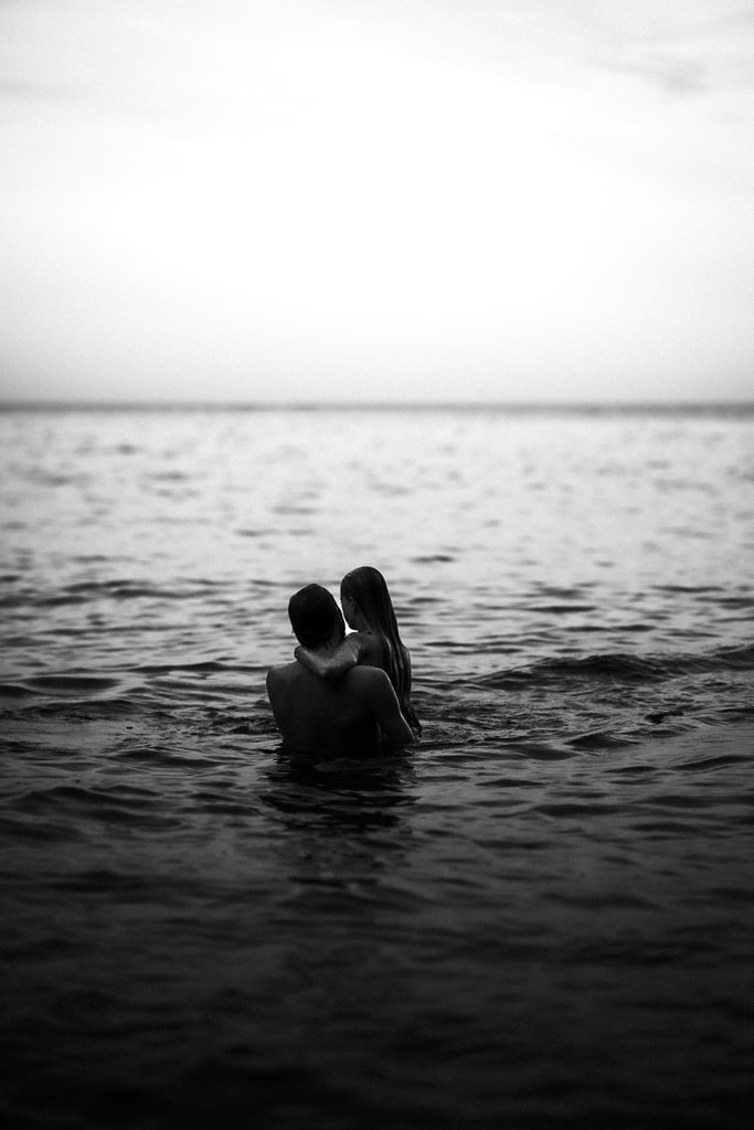 Black and white shot of the couple embracing in the sea, water up to their shoulders, wedding photography in Catalonia