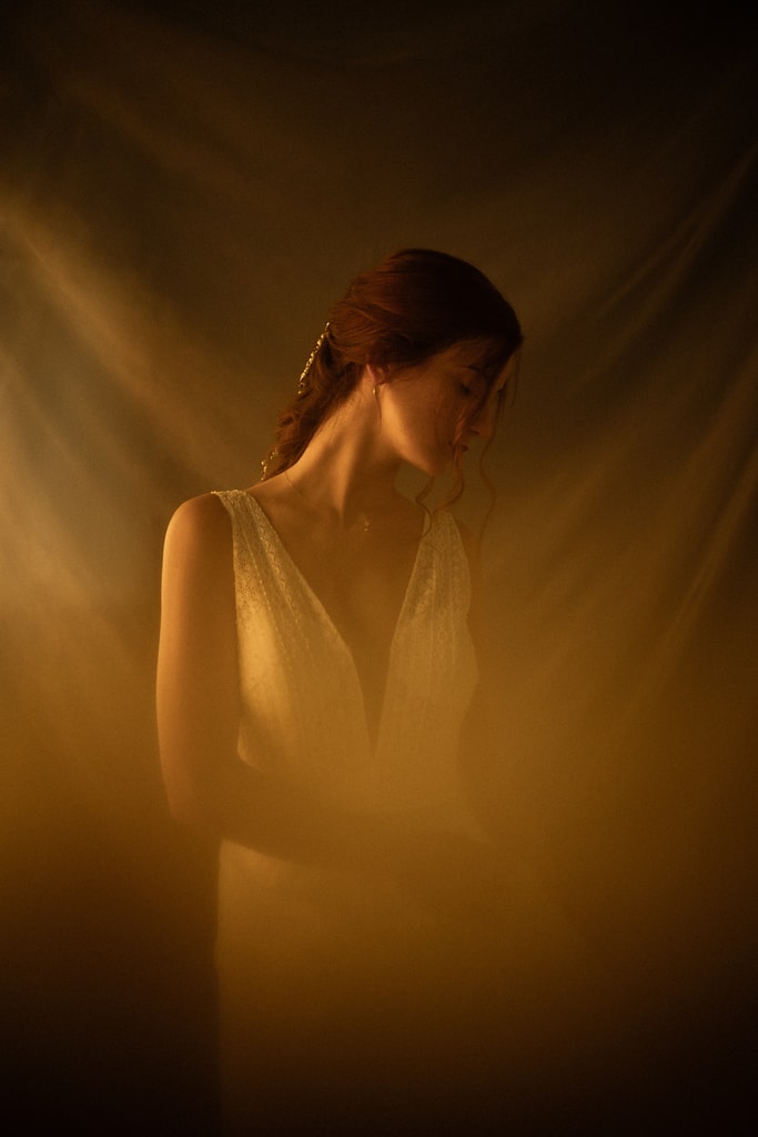 The bride in profile with head bowed, bathed in warm amber light against a dark background, wedding photography in Catalonia