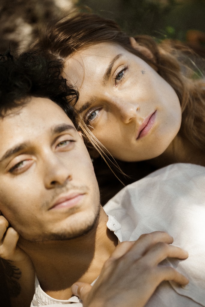 Close editorial portrait of a man and woman cheek to cheek, both looking toward the camera in soft light, wedding photography in Catalonia