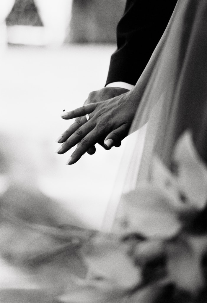 Black and white close-up of the couple’s hands touching, the bride’s veil and flowers in the foreground, wedding photography in Catalonia